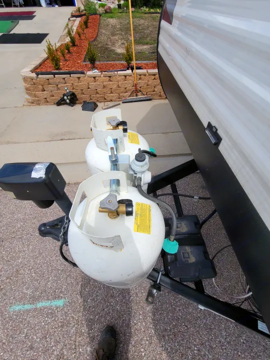 Close-up of two white propane tanks, battery boxes, and the hitch of an RV rental travel trailer. Showing front utilities.. Dutchmen Coleman Lantern 2019