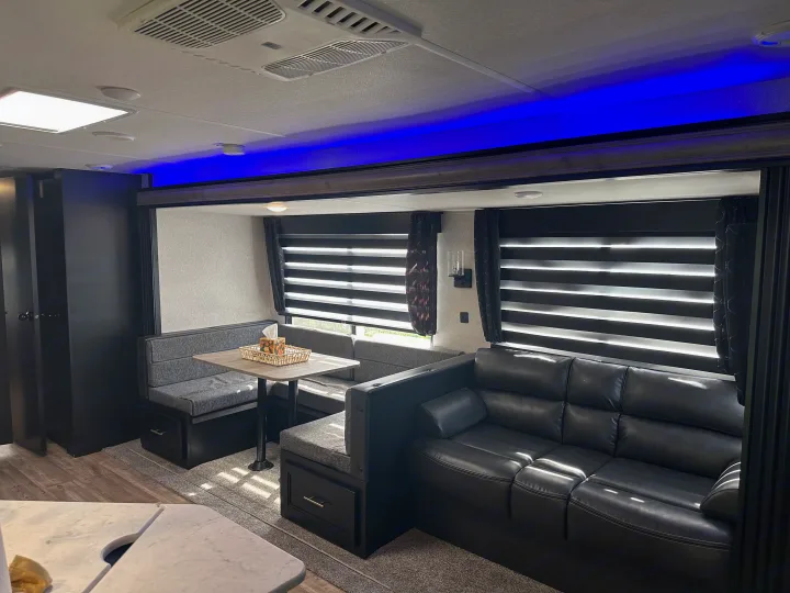 Spacious modern RV rental interior: black leather sofa, dinette with storage, and blue accent lighting.. Forest River Cherokee 2022