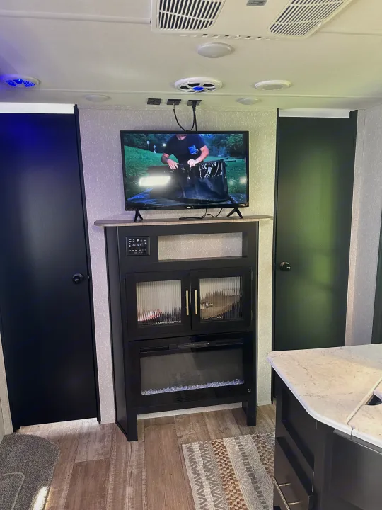 Inside a modern RV rental, showing a well-equipped entertainment center with TV and electric fireplace, plus kitchen counter.. Forest River Cherokee 2022