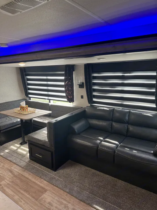 RV rental interior featuring a cozy living space with a black leather sofa, dinette, and bright blue accent lighting.. Forest River Cherokee 2022