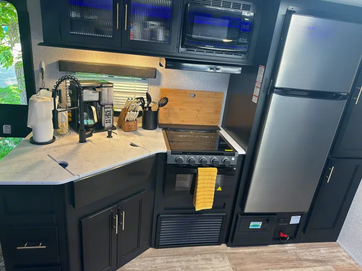 Well-equipped rv rental kitchen: black cabinets, light counter, stainless steel fridge, microwave, stove, and sink area.. Forest River Cherokee 2022