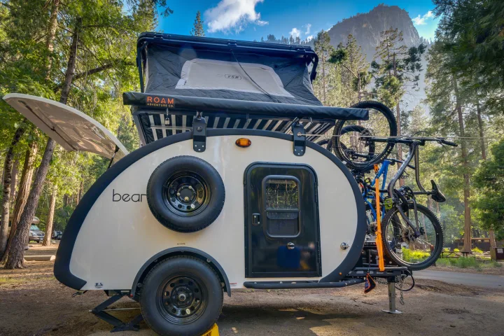 This sleek teardrop RV rental, featuring a rooftop tent and bikes, is set in a scenic forest campground with a mountain view.. Bean Trailer Bean Stock 2022