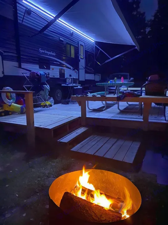 Perfect RV rental camping night: blue lit RV, spacious deck, and a vibrant campfire.. Keystone 27BHS 2017