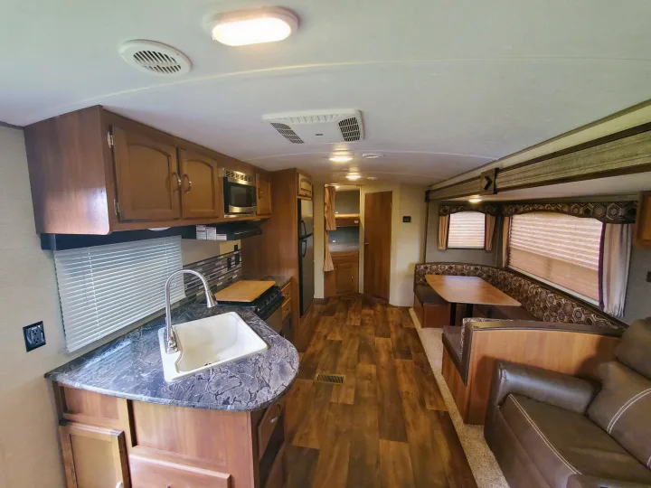 Explore this RV rental's interior: a well-equipped kitchen, dining booth, and comfortable sofa area.. Keystone 27BHS 2017