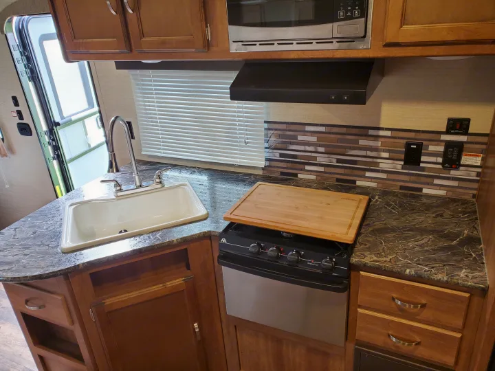 This RV rental features a full kitchen with a sink, stove, microwave, and ample cabinets, perfect for travelers.. Keystone 27BHS 2017