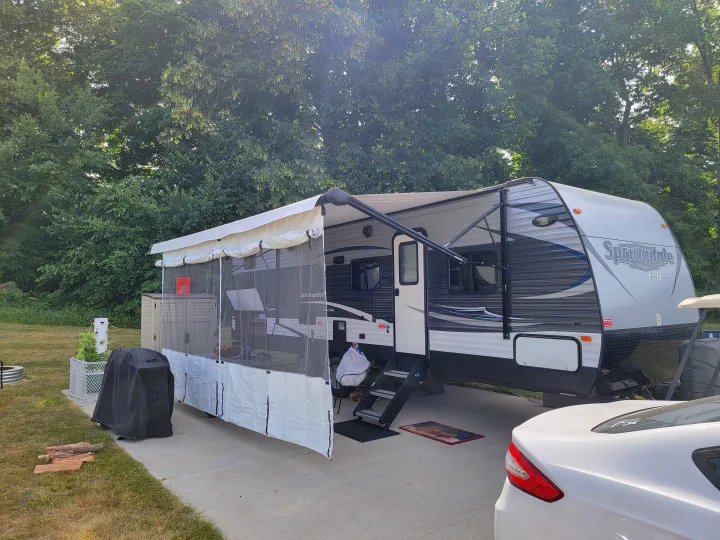 Relaxing at an RV rental campsite with a Springdale camper, screen room, grill, and fire pit setup for outdoor living.. Keystone 27BHS 2017