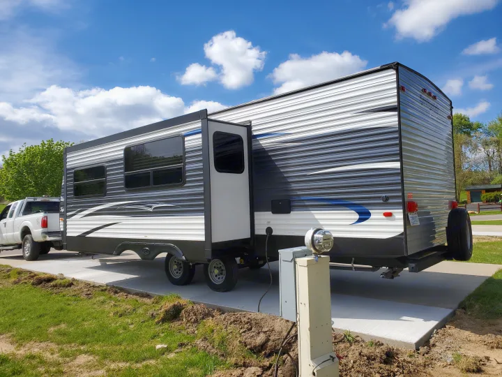 This RV rental is parked on a concrete pad at a campsite, connected to power. A white truck is visible in front of the travel trailer.. Keystone 27BHS 2017