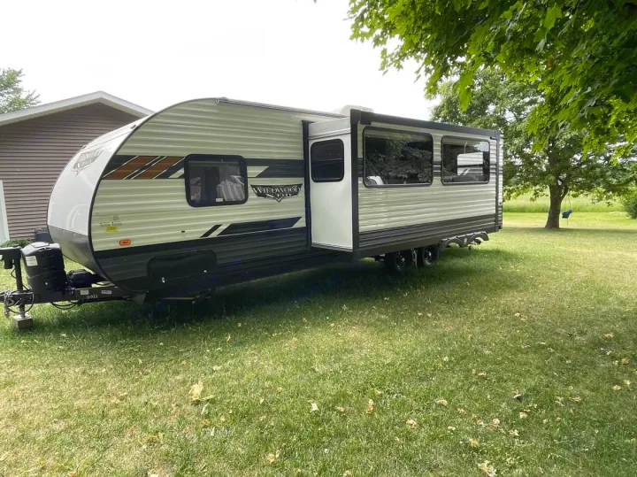 A long travel trailer with an extended slide-out sits on a grassy lawn, ready as an rv rental.. Forest River Wildwood X-Lite 2021