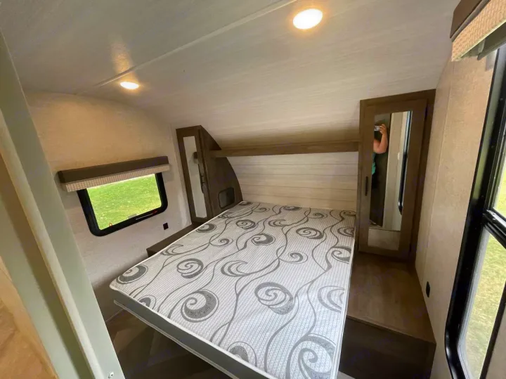 Clean RV rental bedroom: queen bed with patterned mattress, window, and mirrored wardrobe for your travels.. Forest River Wildwood X-Lite 2021
