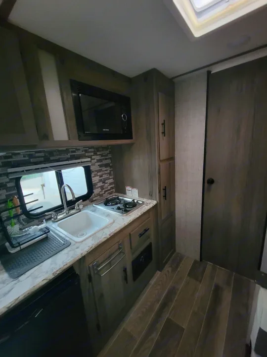Inside an RV rental, this efficient kitchen boasts a sink, stovetop, microwave, and smart storage solutions.. Gulf Stream Ameri-Lite Super Lite 2021