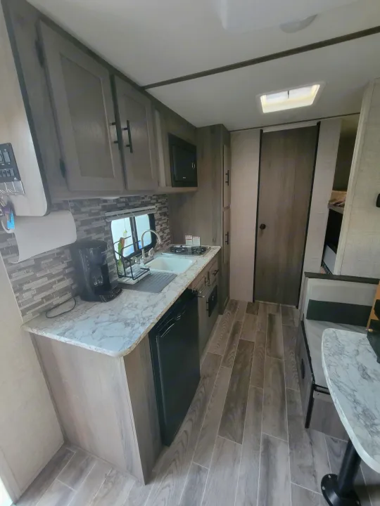 RV rental: Compact kitchen with sink, stove, microwave, fridge, and dining booth. Features wood-look flooring.. Gulf Stream Ameri-Lite Super Lite 2021