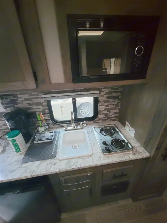 Inside an RV rental: a compact kitchen with sink, stove, microwave, and coffee maker on a patterned counter.. Gulf Stream Ameri-Lite Super Lite 2021