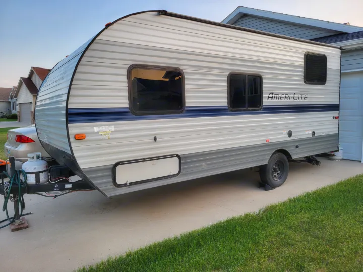 An Ameri-Lite travel trailer, ideal for an RV rental, is parked on a driveway next to a house.. Gulf Stream Ameri-Lite Super Lite 2021