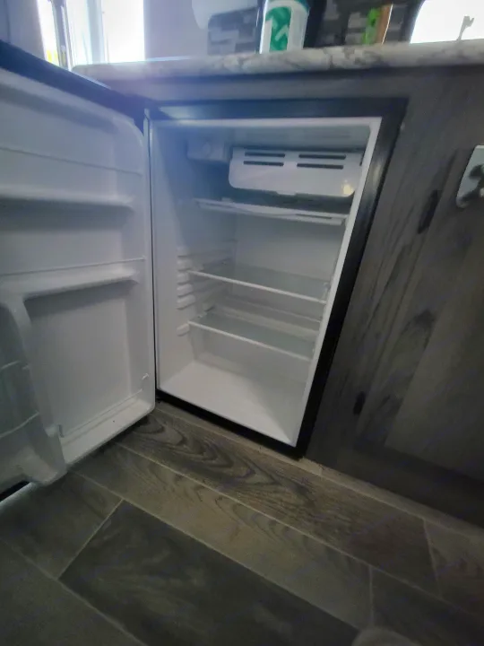 Inside an RV rental: a clean, empty mini-fridge with shelves and freezer, ready for your provisions.. Gulf Stream Ameri-Lite Super Lite 2021