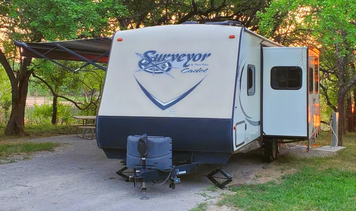 An RV rental, a Surveyor travel trailer, parked at a peaceful campsite with an extended awning and slide-out at sunset.. Forest River Surveyor 2015