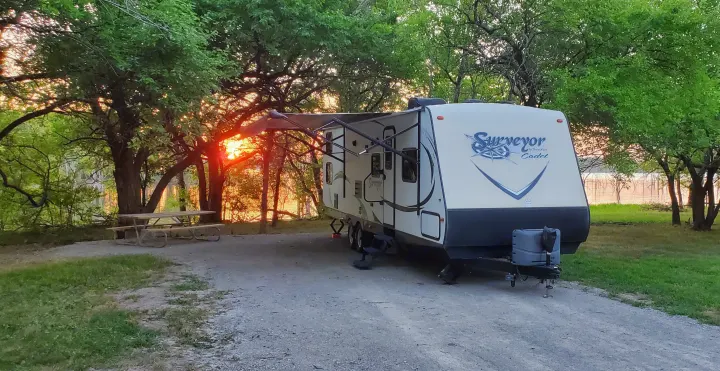 RV rental: A travel trailer parked on a gravel campsite, bathed in warm sunset light with a lake view.. Forest River Surveyor 2015