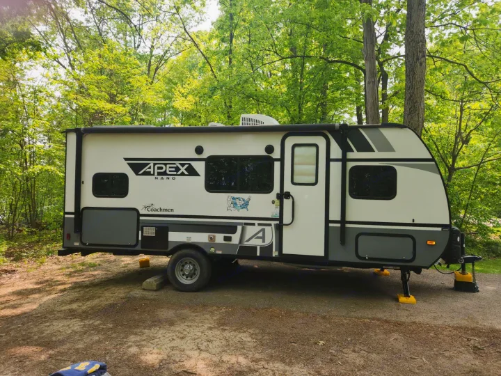 This white/grey Apex Nano Coachmen rv rental travel trailer, displaying US map, is set up in a wooded campsite.. Coachmen Apex Nano 2021