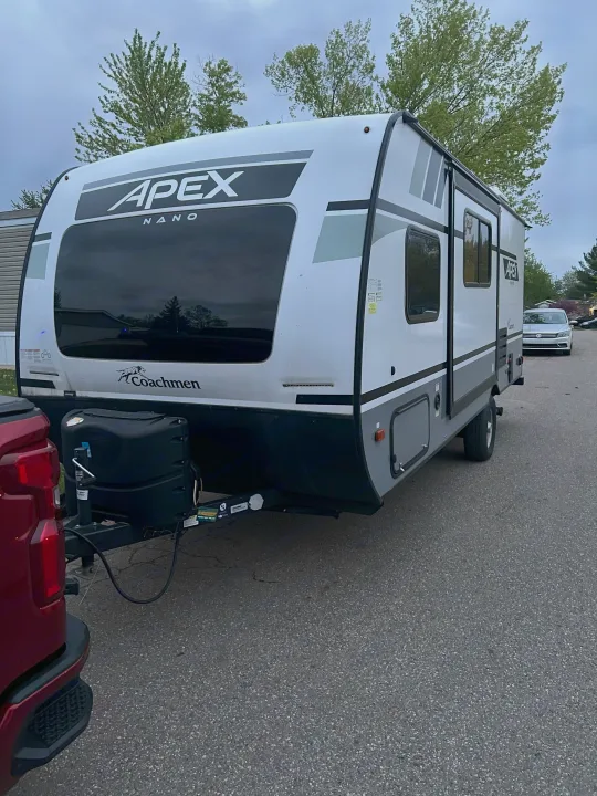 A white Coachmen Apex Nano travel trailer is shown, ideal for an RV rental getaway, attached to a red pickup truck.. Coachmen Apex Nano 2021