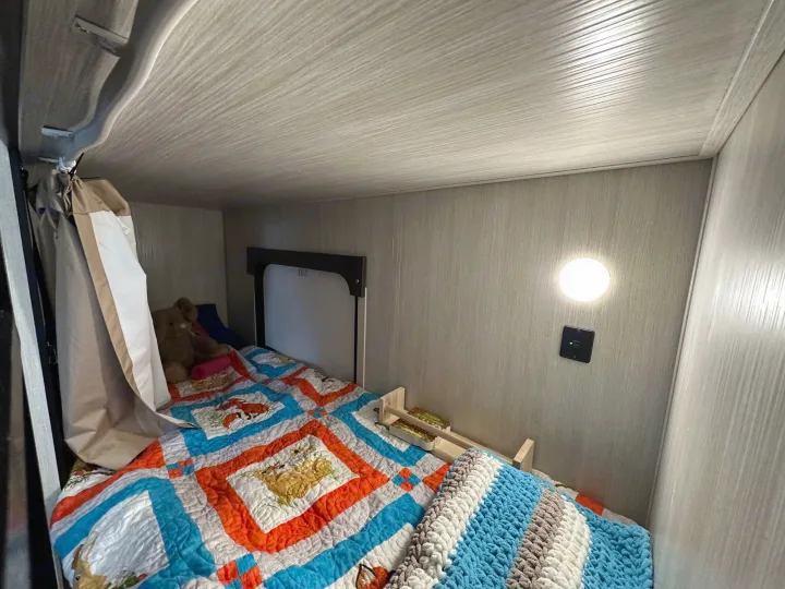 Cozy RV rental bunk bed setup with colorful quilt, plush toy, USB port, and light. Ideal for family travel.. Forest River Cherokee Wolf Pup 2020