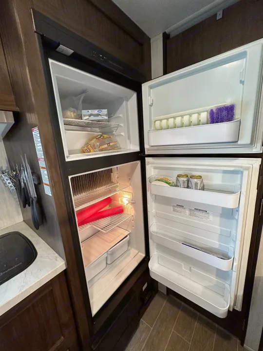 RV rental kitchen: Open refrigerator and freezer show food, drinks, and clever storage inside this compact space.. Forest River Cherokee Wolf Pup 2020