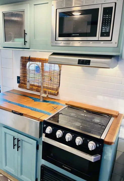 Modern RV rental kitchen with custom wood & resin countertop, microwave, oven, and light blue cabinets.. Forest River Cherokee Grey Wolf 2019