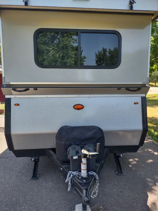 Front view of a compact RV rental featuring a diamond plate storage box, hitch, and side window. Perfect for your trip!. A Liner A Liner Popup Trailer 2022