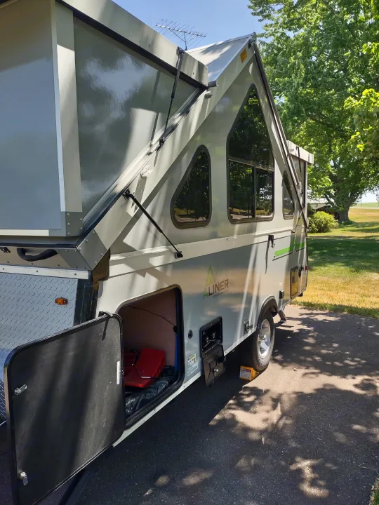 A gray A-Liner folding camper set up outdoors, with open storage. Ideal for an RV rental adventure.. A Liner A Liner Popup Trailer 2022