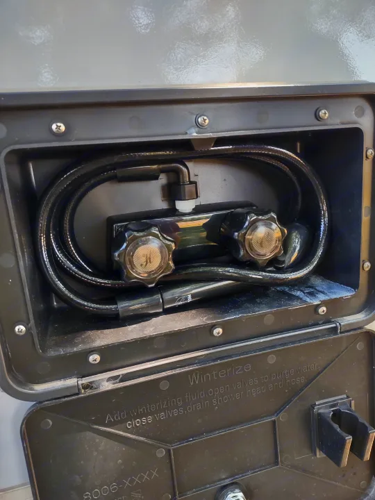 RV rental outdoor shower with hose, knobs, and winterization instructions on the cover, providing convenient exterior water access.. A Liner A Liner Popup Trailer 2022