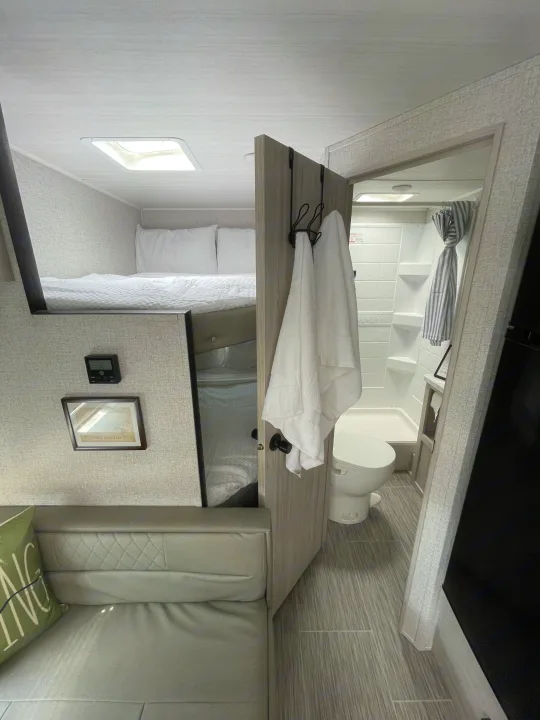 Cozy RV rental interior with an upper bunk bed, sofa, and full bathroom featuring a shower and toilet.. East to West Silver Lake LE 2023