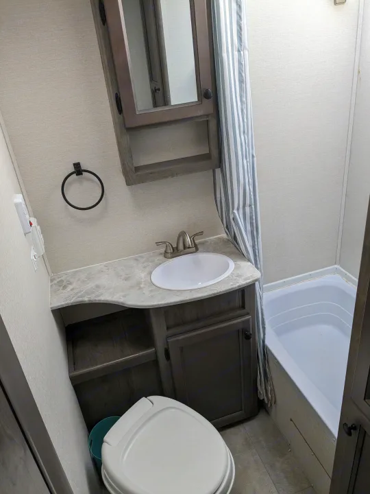 Compact RV rental bathroom: features a toilet, vanity with sink, and small tub with striped shower curtain. Practical space.. Coachmen Apex Nano 2021