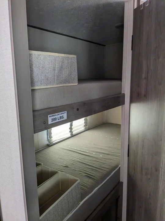 Interior of an RV rental: detailed view of comfortable bunk beds, with the top bunk labeled for a 200 lbs max load.. Coachmen Apex Nano 2021