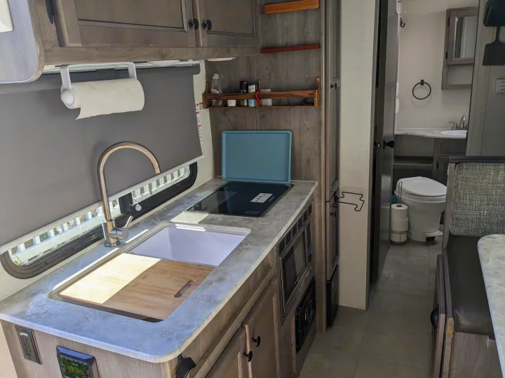 RV rental interior: kitchen with sink, stove, microwave, cabinets & a clear view into the compact bathroom.. Coachmen Apex Nano 2021