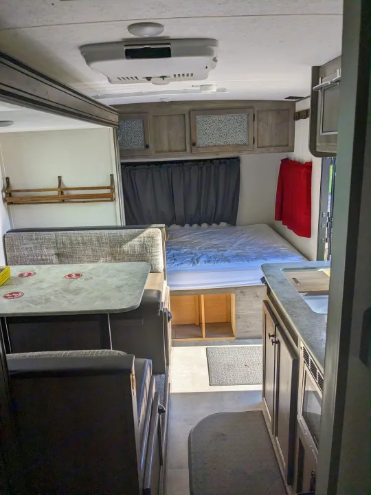Inside an RV rental: dining area, bed, and kitchen. This cozy camper offers a well-appointed, compact living space.. Coachmen Apex Nano 2021