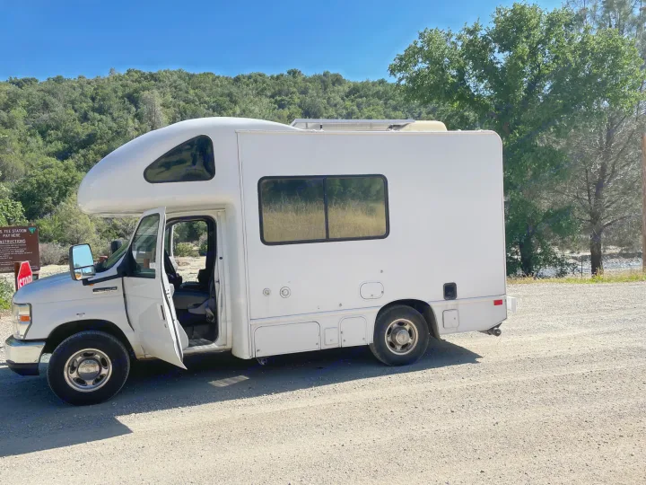 White RV rental (Ford E-350) parked on a dirt road by a river, ready for your next nature adventure.. Four Winds Majestic 2010