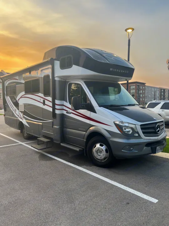 Winnebago View RV rental, a sleek gray & white motorhome, parked with steps extended at golden hour.. Winnebago View 2015