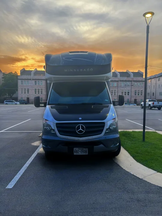 Front view of a Winnebago RV rental parked in a Texas lot under a golden sky.. Winnebago View 2015