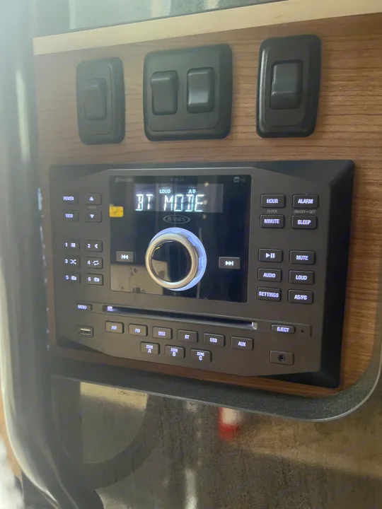 RV rental control panel featuring a Jensen stereo system in "BT MODE" (Bluetooth), with audio controls and light switches.. Winnebago View 2015
