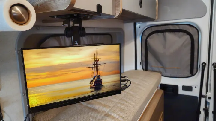 Cozy rv rental interior with ceiling-mounted TV showing a ship on the ocean at sunset, next to a comfortable bench bed.. Winnebago Solis 2023