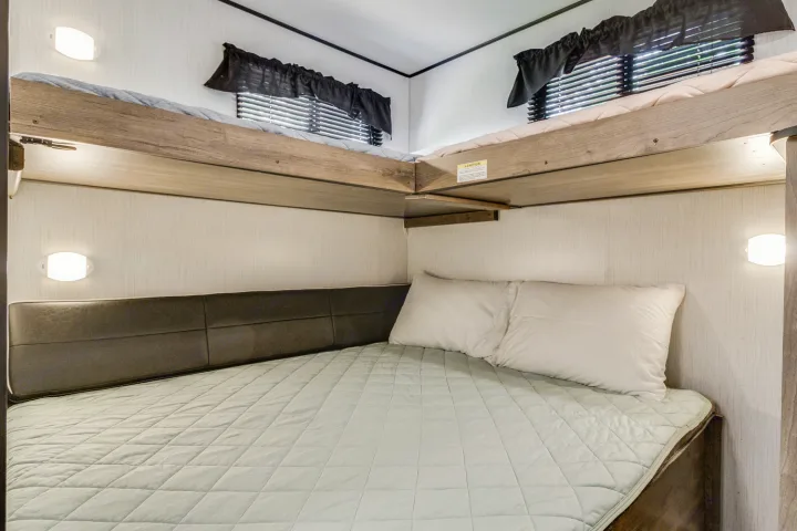 RV rental: Cozy sleeping area. Features a lower bed with two pillows, plus two elevated corner bunk beds above, lit by wall sconces.. Heartland RVs Pioneer 2022