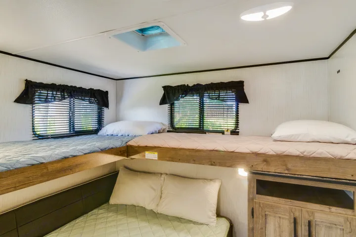 Cozy RV rental bunk beds, perfect for family adventures. This camper interior features two upper bunks, a lower bed, and windows.. Heartland RVs Pioneer 2022