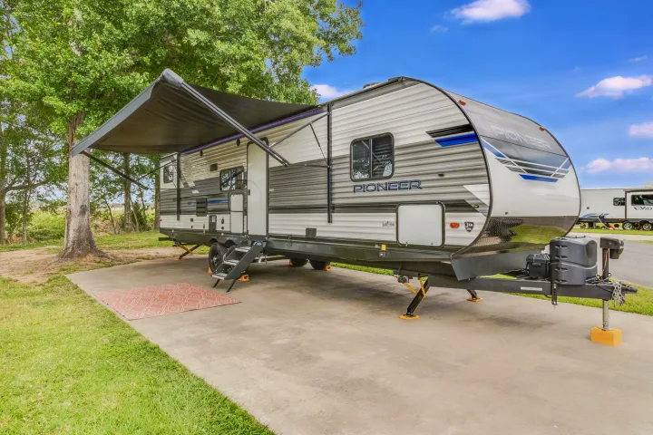 Spacious gray & white RV rental set up at a sunny campsite with its awning extended, perfect for outdoor relaxation.. Heartland RVs Pioneer 2022