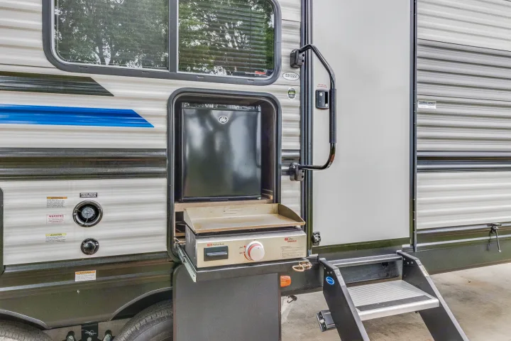RV rental: Side view showing an outdoor kitchen with a griddle & mini-fridge, water hookups, and entry steps.. Heartland RVs Pioneer 2022