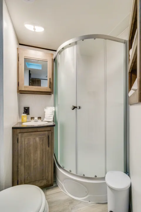 Modern RV rental bathroom features a corner shower, vanity with sink, medicine cabinet, and toilet.. Heartland RVs Pioneer 2022