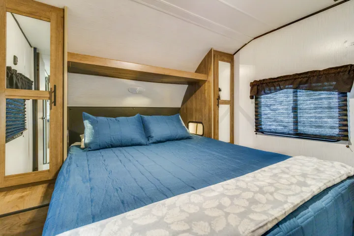 Cozy RV rental bedroom featuring a blue bed, mirrored closet, and window. Ideal for compact living.. Heartland RVs Pioneer 2022