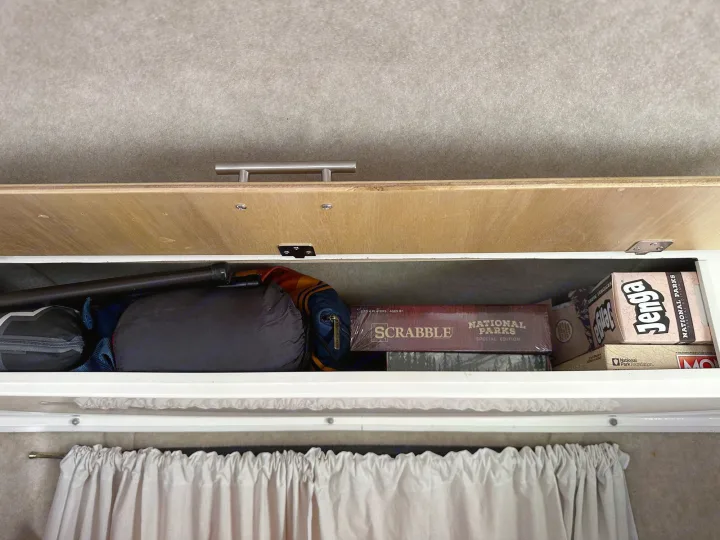 Inside an RV rental's overhead cabinet: organized camping gear, Scrabble, and Jenga National Parks games for travel fun.. Scamp Scamp Trailer 2010