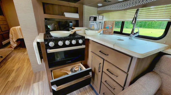 Well-equipped RV rental kitchen with stove, sink, and coffee maker, perfect for road trips. Open drawer shows storage.. Thor Freedom Elite 2021