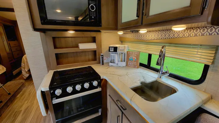 This RV rental kitchen boasts a stove, microwave, sink, coffee maker, and ample counter space for travel.. Thor Freedom Elite 2021