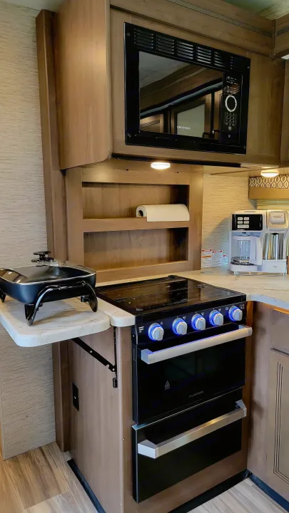 Modern RV rental kitchen featuring a GREYSTONE microwave, FURRION stove with blue lit knobs, and a coffee maker.. Thor Freedom Elite 2021