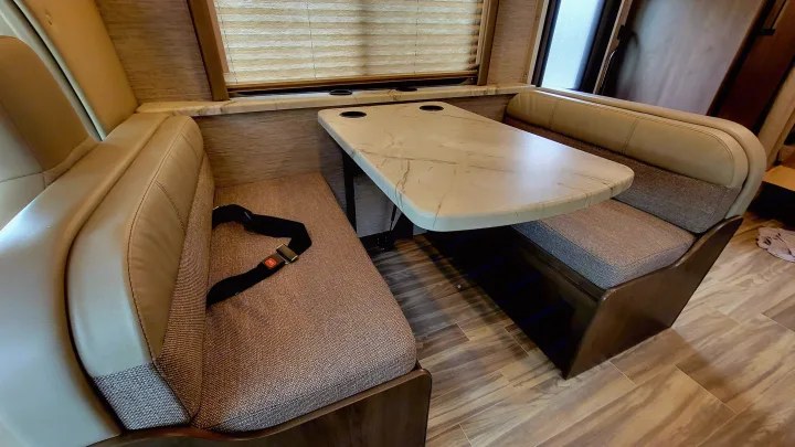 RV rental: Bright dinette area with tan benches, marble-look table with cup holders. Seatbelt on left bench. Wood-grain floor.. Thor Freedom Elite 2021