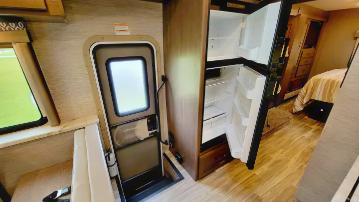 Explore this RV rental's interior: open fridge, main entry, living area, and a glimpse of the bedroom.. Thor Freedom Elite 2021